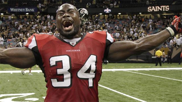 Ovie Mughelli celebrating in a red Falcons number 34 jersey with his arms extended